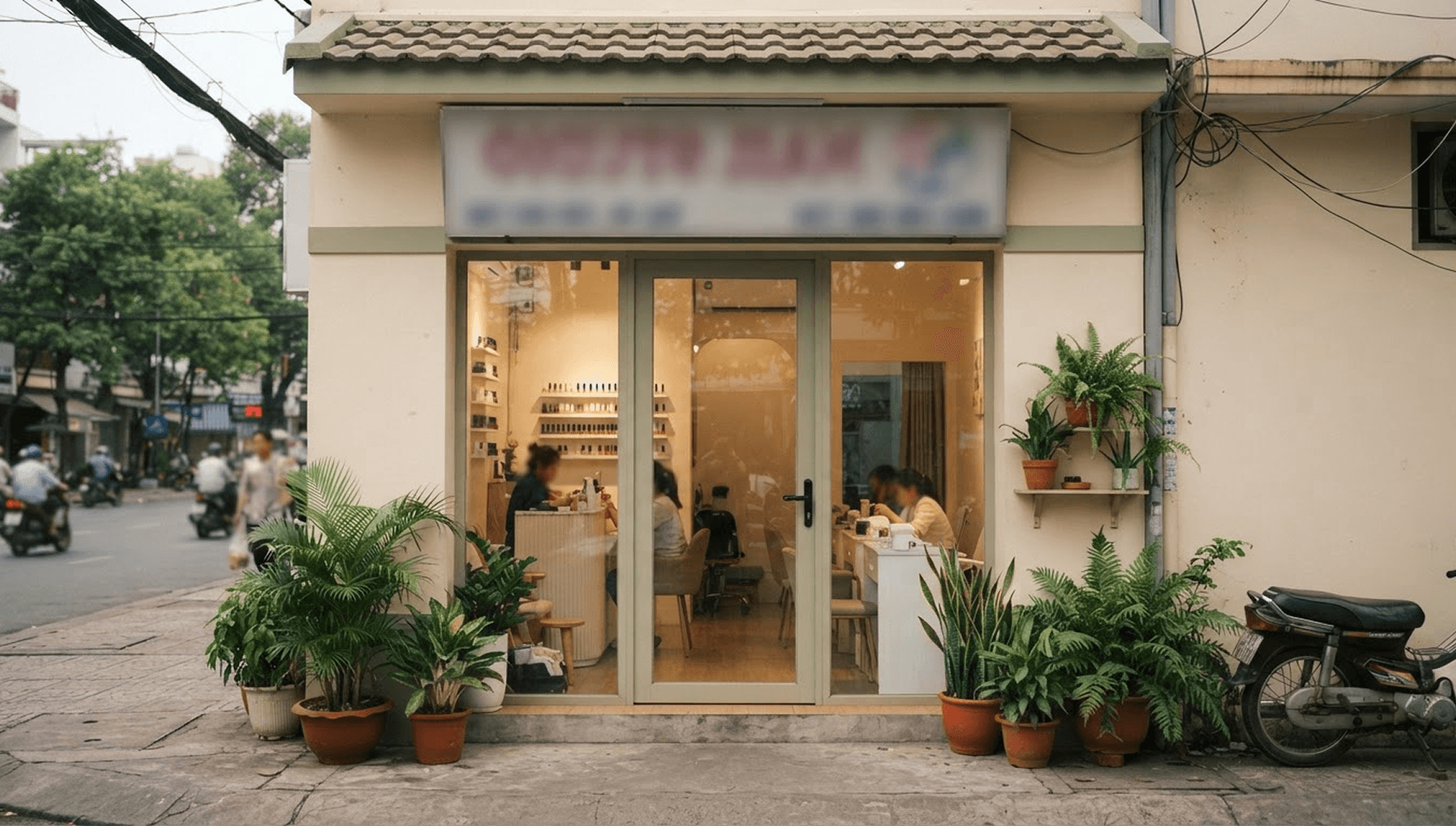 Mặt tiền tiệm nail nhìn từ vỉa hè đối diện, cửa kính và lối vào ở giữa khung hình
