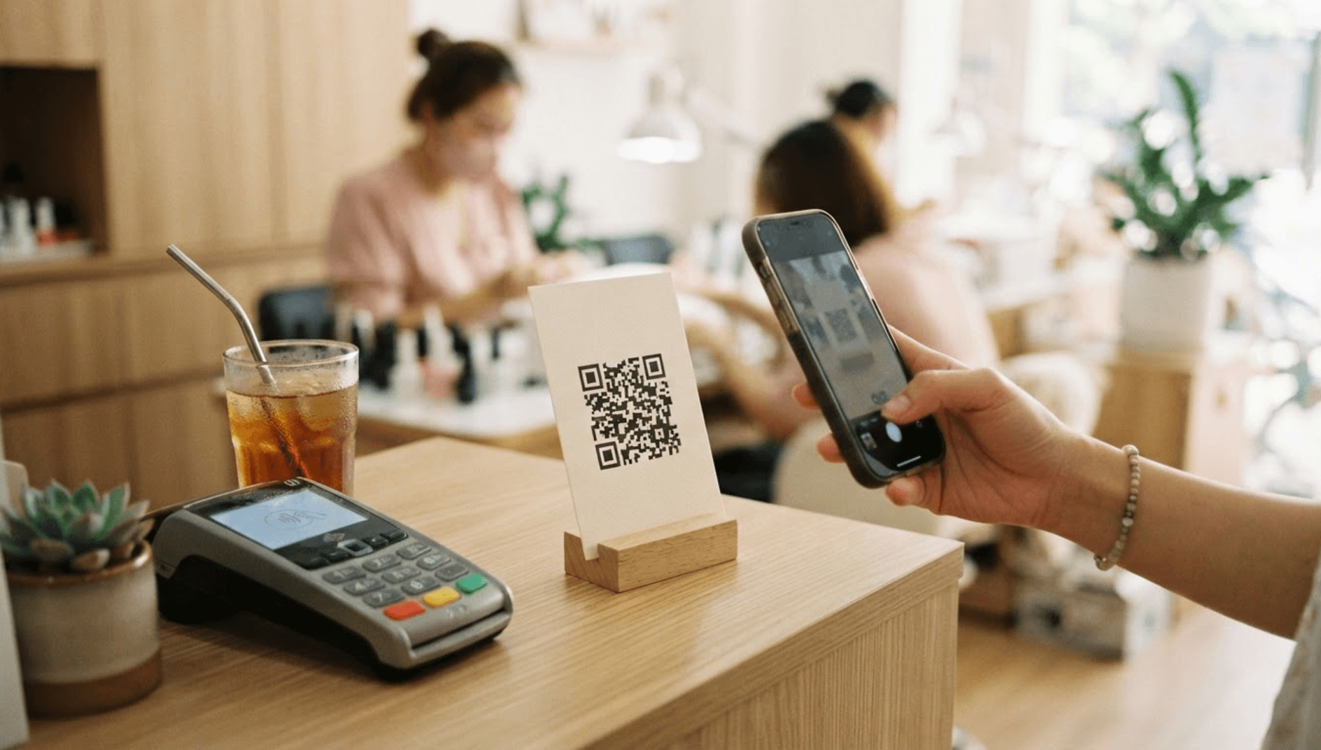 Tấm thẻ in mã QR đặt cạnh máy thanh toán, tay khách đưa điện thoại về phía thẻ